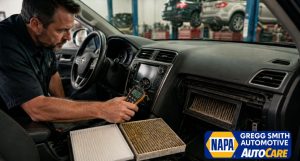 Mechanic inspecting car airflow in Gregg Smith Automotive with clean and dirty cabin filters on the passenger seat.